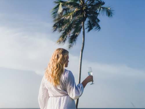 the bahamas woman in white long sleeve shirt holding white ceramic mug standing beside palm tree during daytime tropical